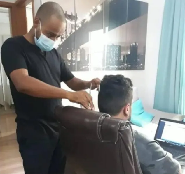 Eliabe cortando o cabelo de um cliente sentado na cadeira do escritório, em casa