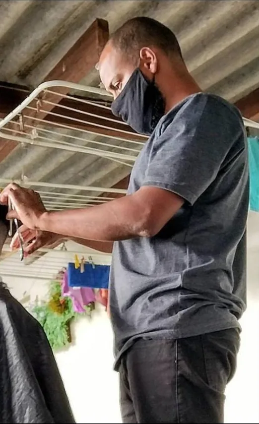 Eliabe cortando o cabelo de um cliente na varanda de uma casa